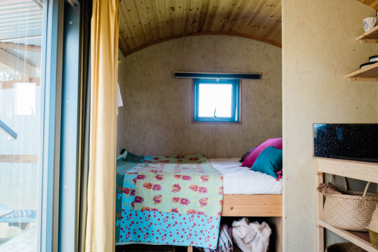 Cosy double bed with colourful bedding in wooden Shepherd's Hut