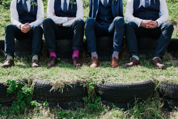 Groom and groomsmen in suits sat on tyres in sunshine