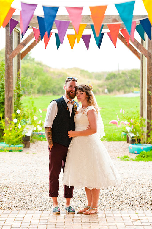 Bride and groom on wedding day beneath colourful bunting decoration