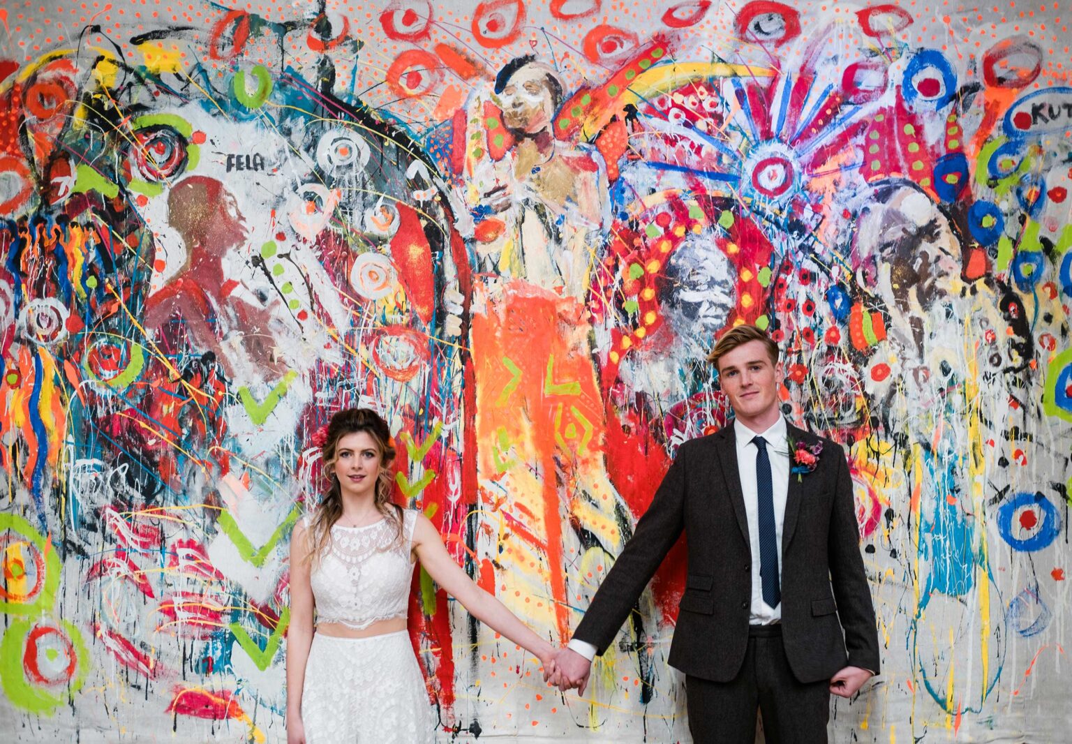 Bride and Groom holding hands in front of brightly coloured backdrop